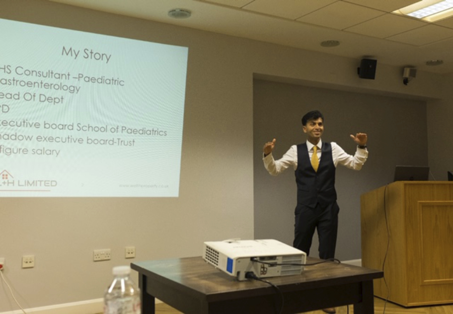 Dr Prithvi Rao, an Indian man, at the front of a lecture theatre, giving a presentation about his property investment journey
