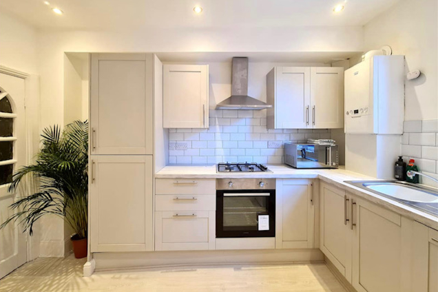 Refurbished kitchen with modern pale grey units, white worktop, stainless steel appliances and laminate flooring