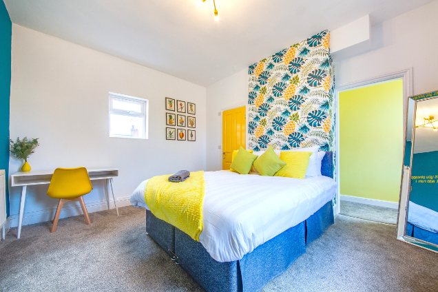 Double bedroom with pineapple wallpaper feature wall, blue and yellow soft furnishings and white Scandinavian style furniture