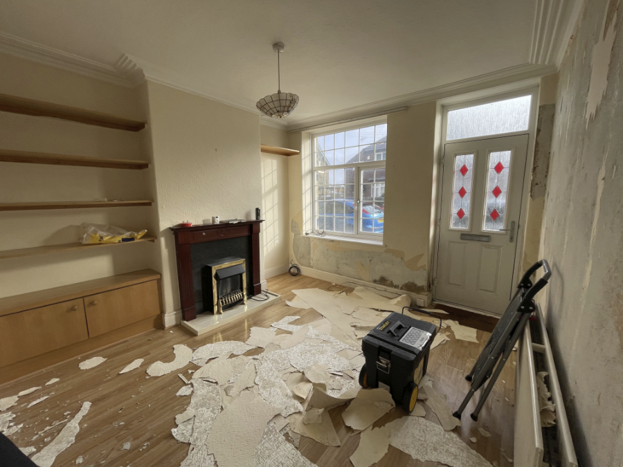 A dated living room mid redecoration. Textured wallpaper stripping is in progress and there are pieces all over the floor